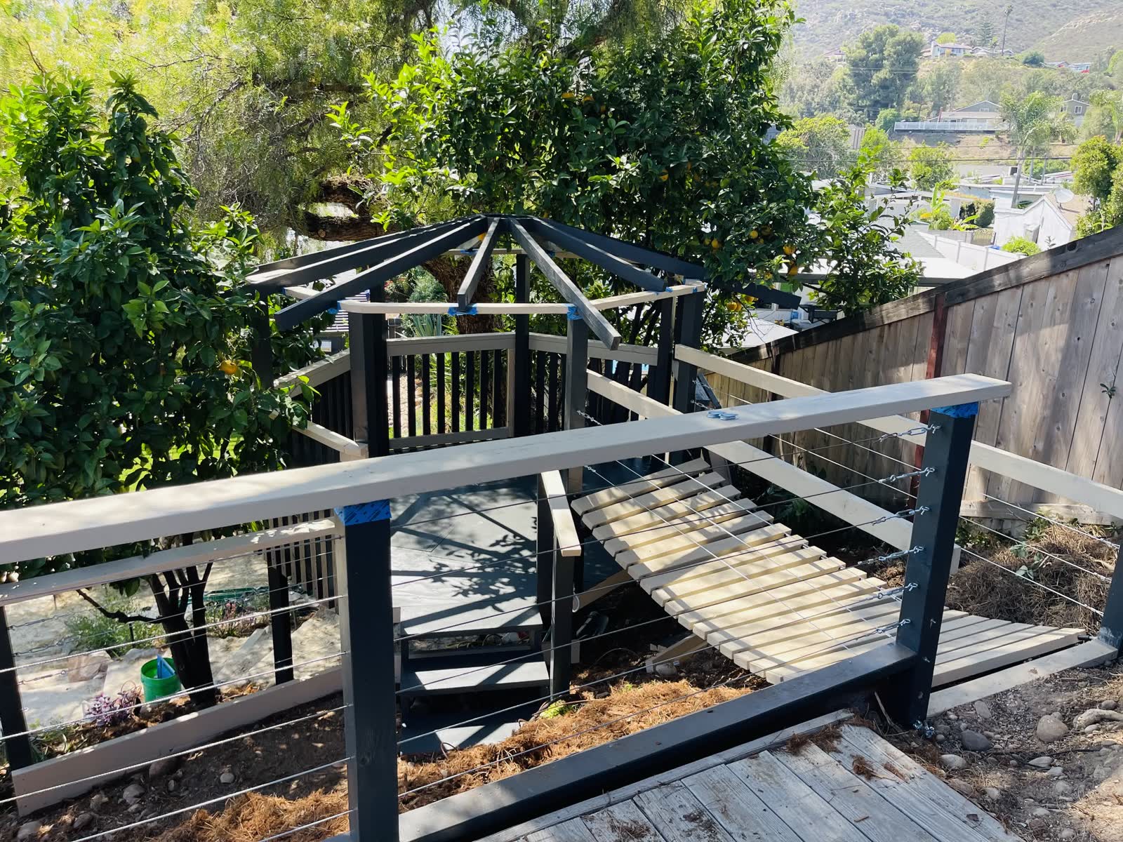 Hexagonal cedar gazebo with cable railing and a custom arched slat bridge built into a hillside