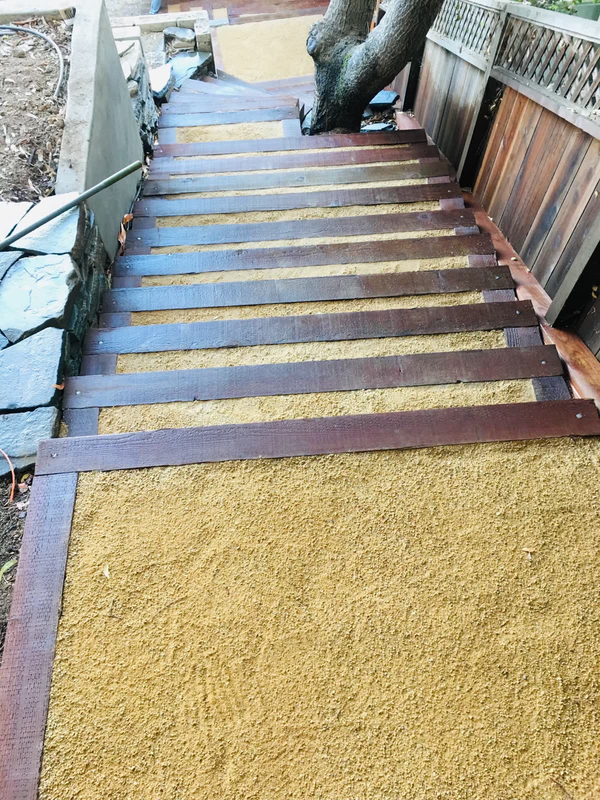 Stained wood slat steps set into decomposed granite on a hillside beside a stone wall