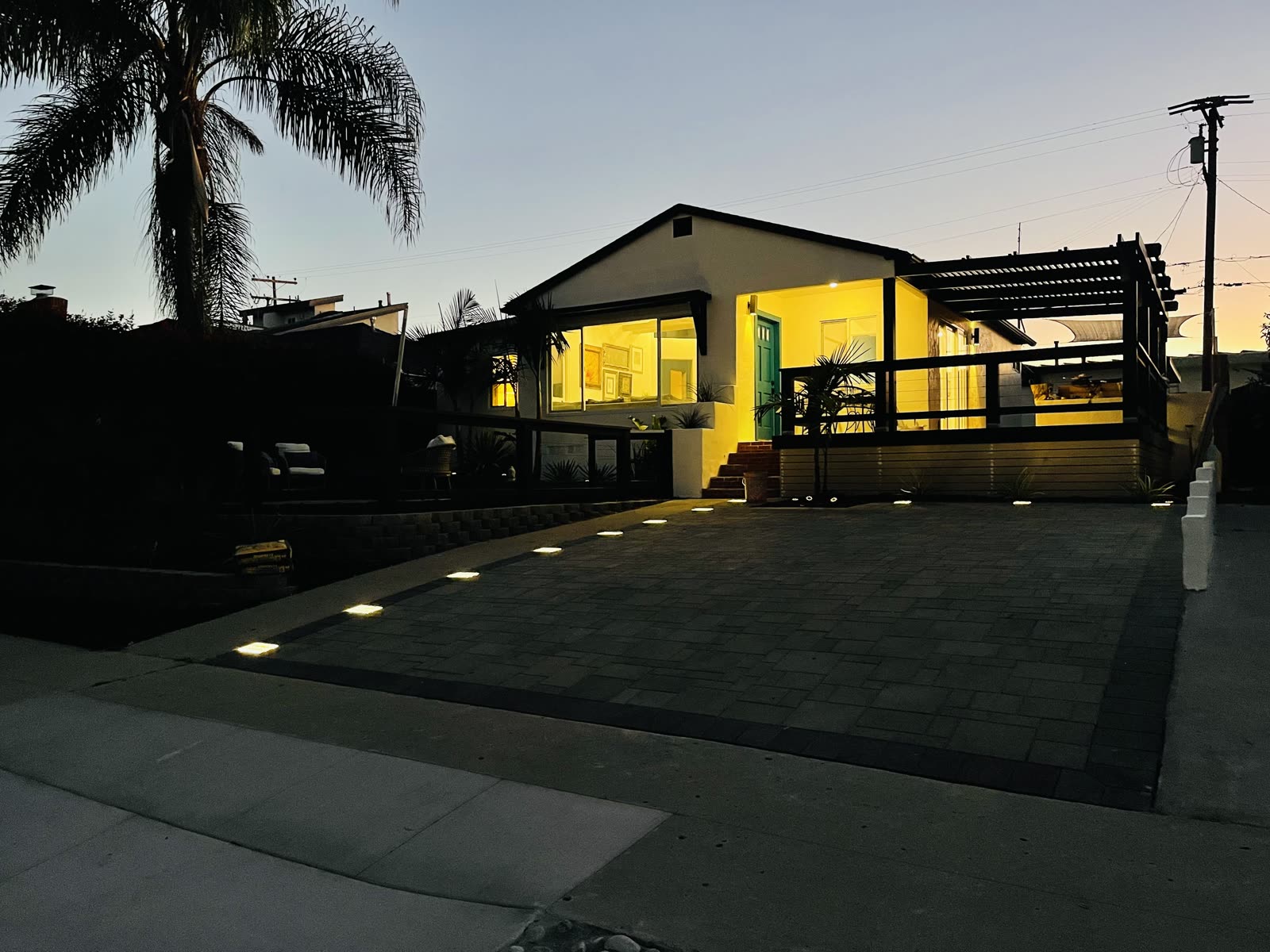 Paver driveway lit by recessed low voltage lights at twilight beside a black pergola