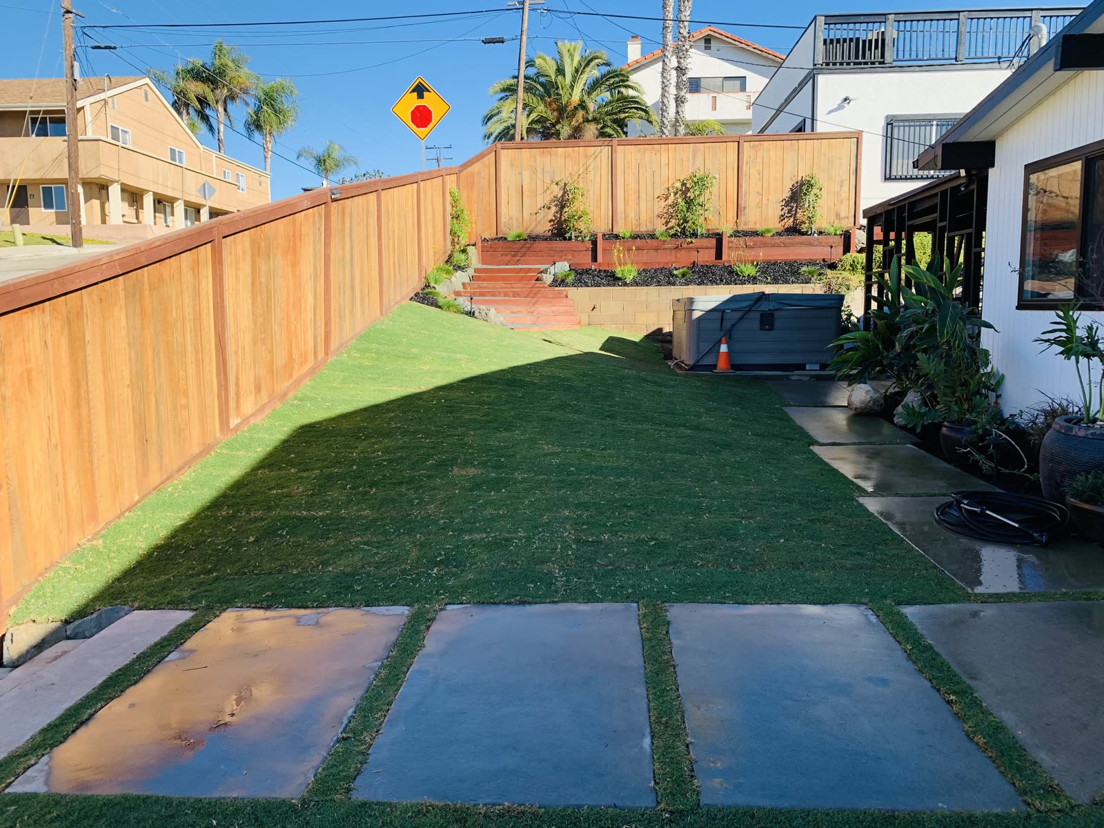 Backyard with redwood fencing, lawn, concrete paver walkway, and tiered redwood planter boxes