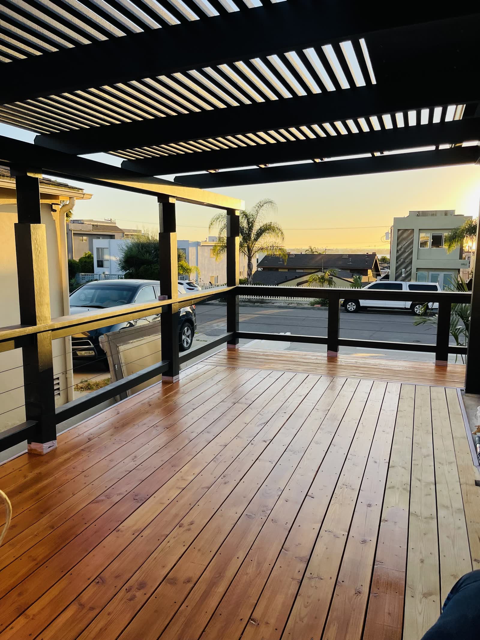 New redwood deck under a black louvered pergola with cable railing at sunset